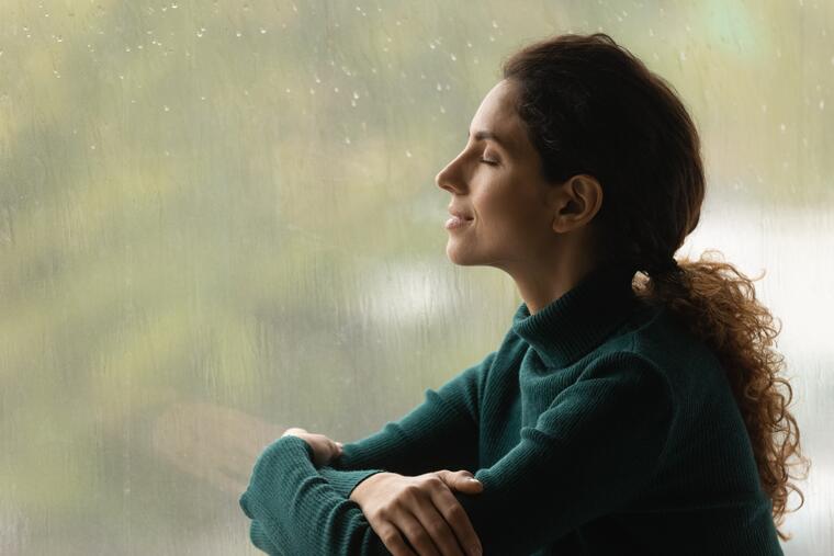 Woman with closed eyes sitting in front of the window