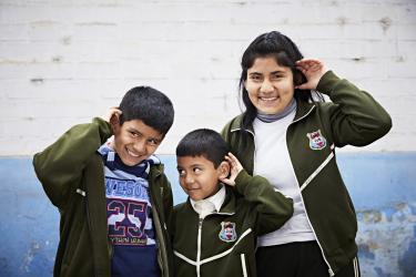 three siblings in Peru in the Hear the World pose (hand cupped behind the ear)